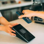 Close-up of a hand holding a smartphone to scan a QR code on a card payment terminal