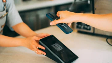 Close-up of a hand holding a smartphone to scan a QR code on a card payment terminal