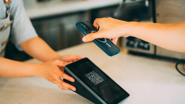Close-up of a hand holding a smartphone to scan a QR code on a card payment terminal