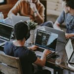Five people collaborating on laptops around a wooden table in a coworking space