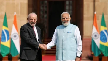 Prime Minister Narendra Modi and Brazilian President Luiz Inácio Lula da Silva shaking hands warmly in front of the Indian and Brazilian national flags at Hyderabad House in New Delhi