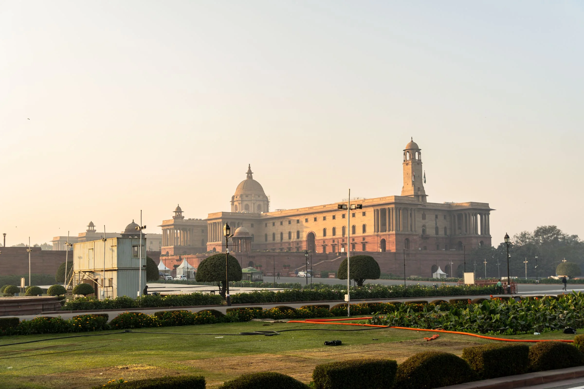 Wide view of the sandstone Secretariat building and manicured lawns in New Delhi under a clear sunrise sky