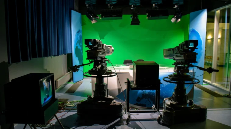 Two professional broadcast television cameras with teleprompters facing an anchor desk in a modern newsroom studio