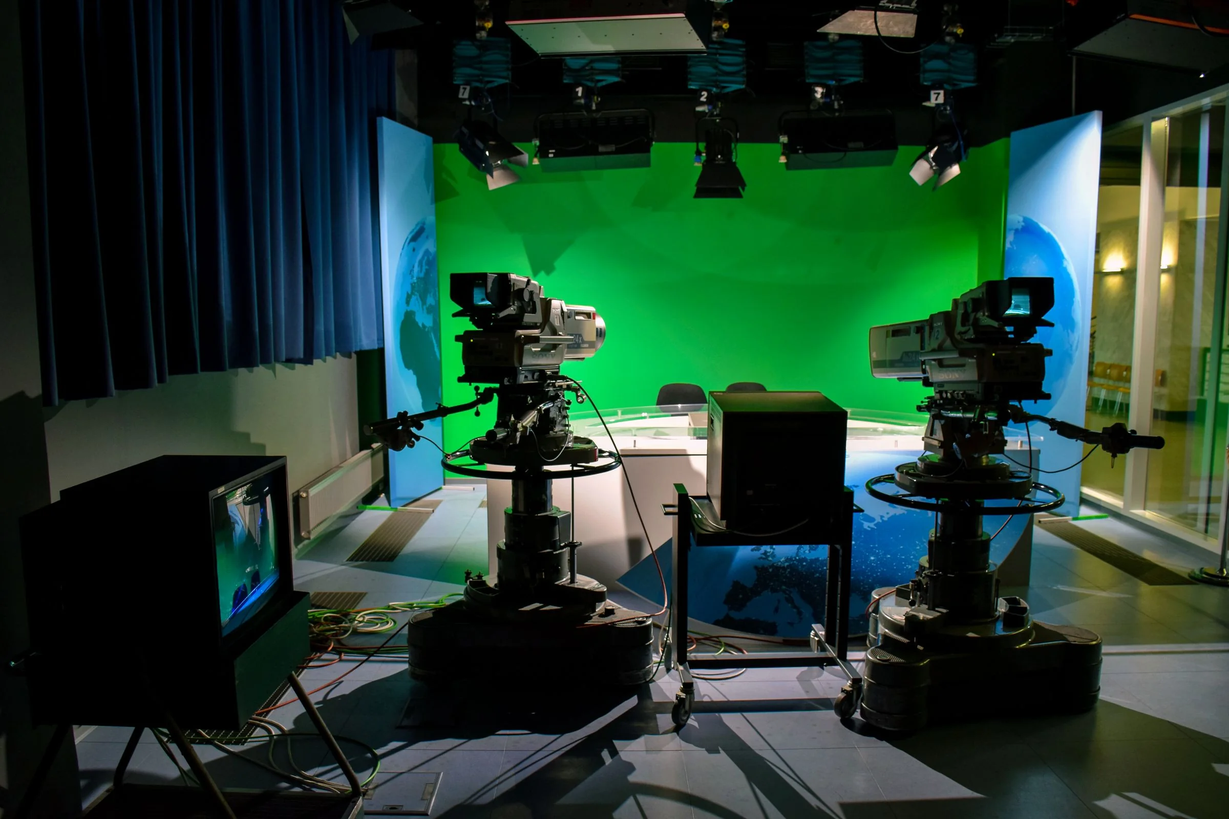 Two professional broadcast television cameras with teleprompters facing an anchor desk in a modern newsroom studio