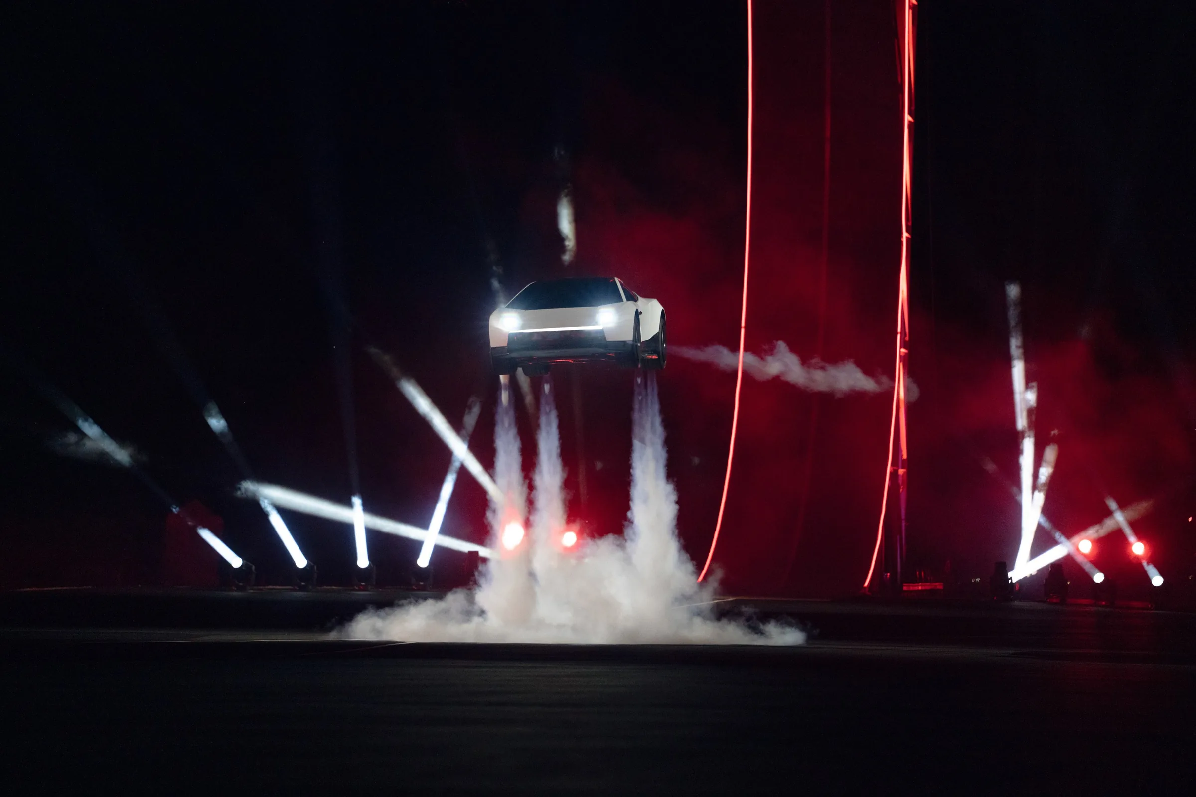 The new white Tesla Roadster hovering above the ground on columns of white cold-gas exhaust, lit by red and white stage lights at night