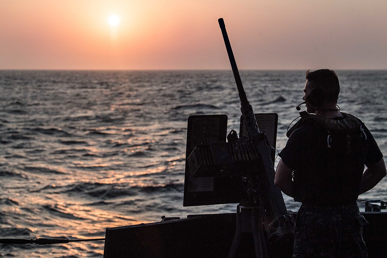 Sailor on watch aboard a naval ship at sunset in a strategic strait